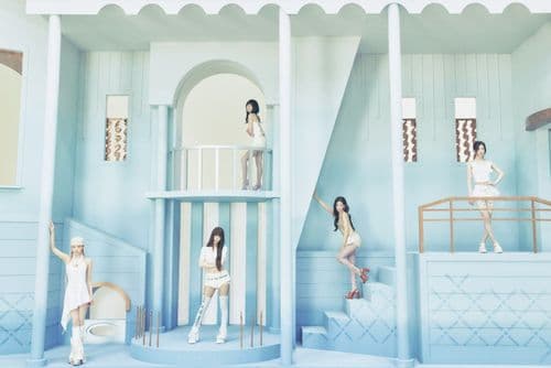 Five women in light attire pose within a whimsical, multi-level light blue dollhouse set.