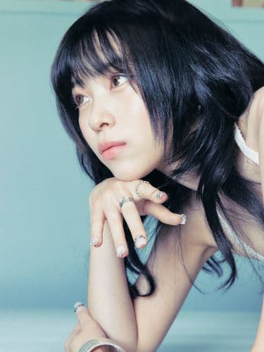 Close-up of a woman with dark hair, looking thoughtful, wearing rings on her fingers.