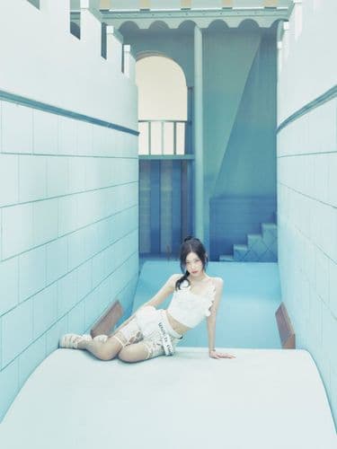 Woman in a white outfit sitting on a white platform in a light blue, tunnel-like room.