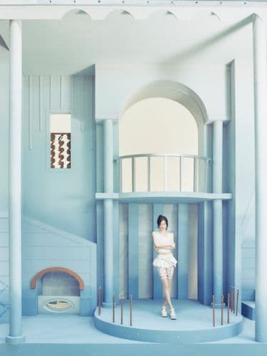 Woman in white outfit standing on a circular platform in a multi-level blue architectural space.