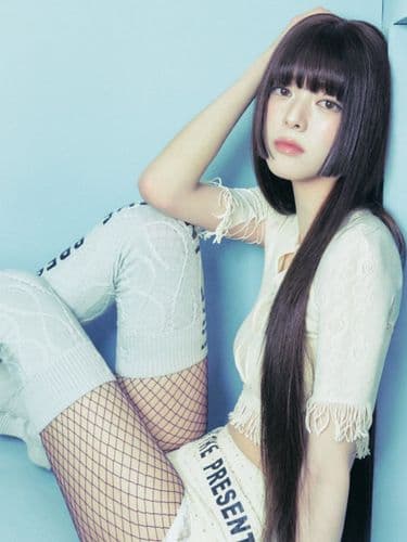 Woman with long dark hair and bangs wearing white top, shorts, and fishnet stockings.