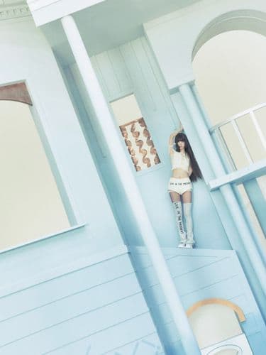 Woman in white crop top and shorts stands in a minimalist light blue architectural interior.