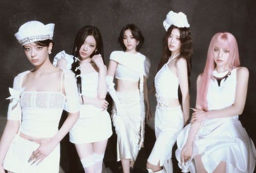 Five women in various white outfits pose together, two with hats, against a dark backdrop.