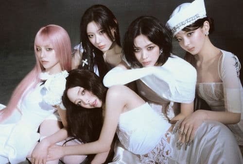 Five women in white outfits in a close-up group pose, some seated, against a dark background.