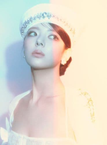 Woman with short dark hair, wearing a white embellished hat, looking up with soft lighting.